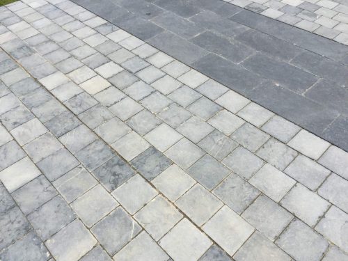 Detail of grey bluestone tumbled paving stones laid in a linear pattern for an outdoor driveway or terrace